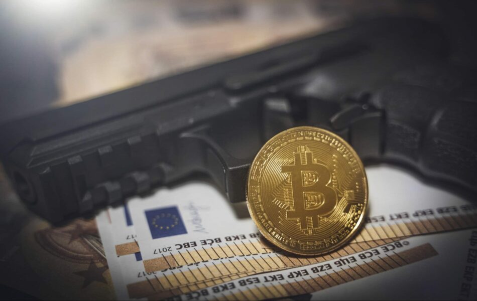 Pistole neben Euro-Noten und Bitcoin-Münze.